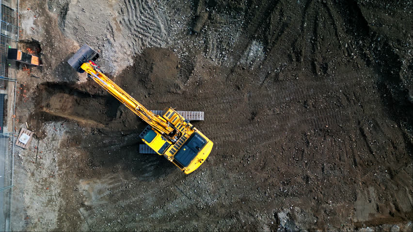 Static aerial top down view of excavator rotating on tracks in construction site