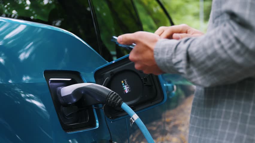 Close up Man plugging an electric car or EV at charging station at green. Save ecology alternative energy sustainable of future.