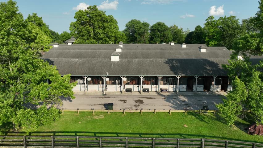 Kentucky Horse Park. Equestrian facility with a row of stalls under a slate roof. Lush trees surround the area while the clear blue sky is overhead. Aerial shot of Kentucky