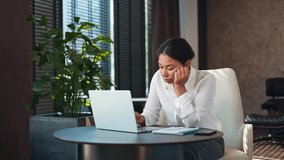 Sad african american woman with boring facial expression typing lazily on wireless laptop at modern workplace. Tired female office worker in white blouse feeling lack of inspiration at unloved job. - Powered by Shutterstock - Get 15% off with code: PIKWIZARD15