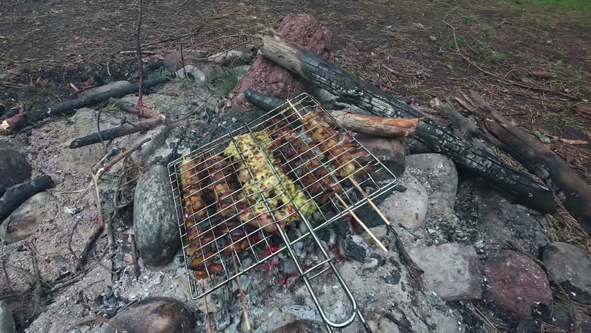 POV shot during the barbecue with a grill grate on which shashlik skewers with delicious meat and vegetables are skewered grilled on a hot coal fire built with stones Royalty-Free Stock Footage #1110373031