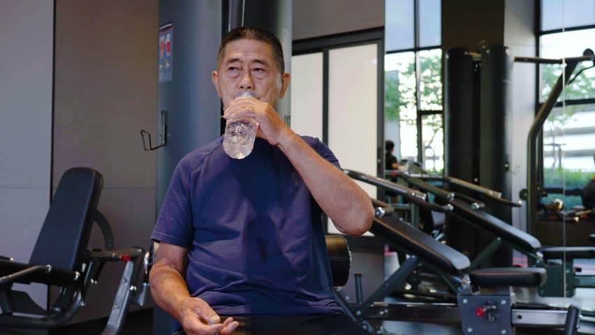 Asian elderly old man in the 70s or 80s drinking water after doing exercise in the gym - a health senior lifestyle, Healthy lifestyle, Sport activity