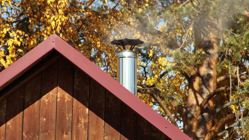 Smoke comes from pipe on the roof of a private house against the backdrop of an autumn forest, heating a residential building in autumn, lifestyle