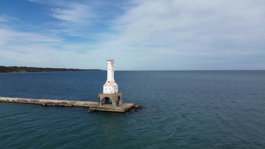 Port Washington lighthouse on Lake Michigan. Aerial flyover shot at the top level of the lighthouse that rotates around it, showing the pier, shoreline, and downtown areas.