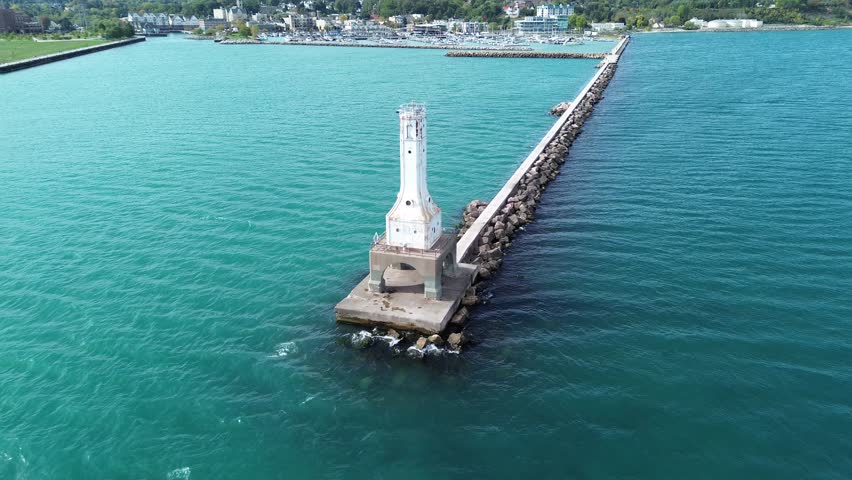Port Washington lighthouse on Lake Michigan. Aerial flyover shot from the lighthouse towards the shore, along the pier. Visible in the background are downtown businesses and the harbor.