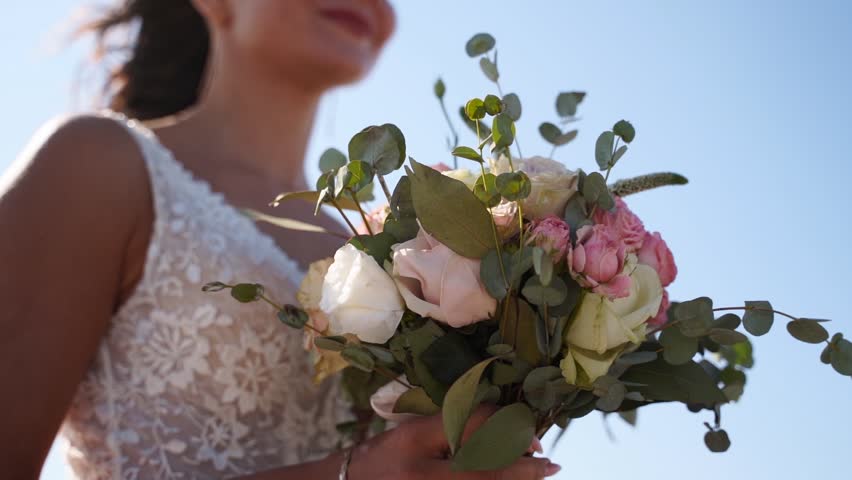 Elegance bride holding wedding bouquet at photoshoot. Young attractive woman with delicate flowers posing after wedding ceremony. Lady with pink and white roses in a gorgeous wedding dress. Close-up.