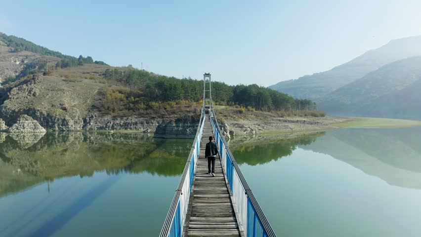 Aerial view of a man walking on a bridge over the Studen kladenec dam in Bulgaria, with mountains in the background