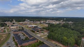 descending aerial footage of Grambling State University with red brick buildings surrounded by green trees and grass, cars driving on the street, blue sky and powerful clouds in Grambling Louisiana