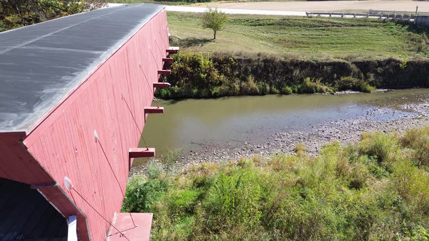 Hogback covered bridge in Madison County Iowa. Aerial flyover shot, closeup, along side of bridge and across the stream below. Shot features the bracing and trussing design of the bridge.