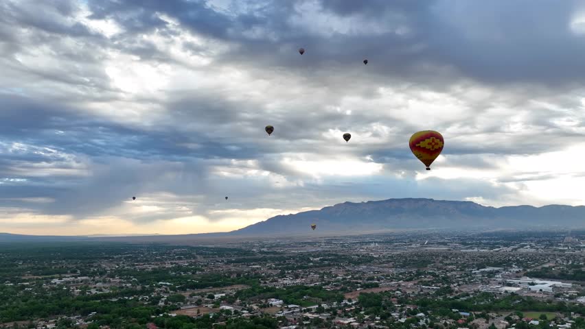 Hot air balloons soar over Albuquerque, with a stunning mountain vista and clouded skies, showcasing the city
