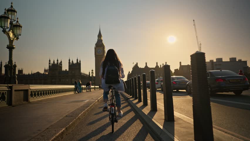 Cinematic shot young tourist woman riding bicycle on Westminster Bridge London towards Big Ben at sunset. Concept of tourism cycle sport activity in London Royalty-Free Stock Footage #1110402941