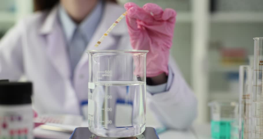 Scientist holds neutral litmus paper on test tube with sample of natural drinking water in laboratory. Checking quality of water purity