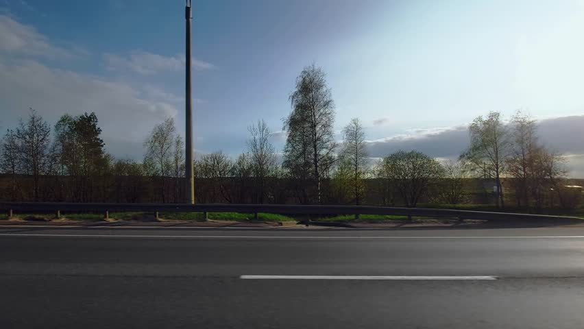 Highway out of town. Three lane freeway. Traffic barrier guard rail along roadway. View through side window on passenger seat of car in motion. Spring in april, evening. Field, trees on background Royalty-Free Stock Footage #1110406959