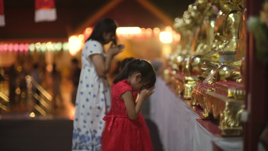 Happy Asian family, mother and children paying homage Buddha in temple to make a wish on the traditional Loy Krathong or Songkran festival in Thailand.