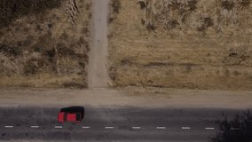 The drone flies over a country road surrounded by steppe and bushes. Cars of different colors are driving along the road.