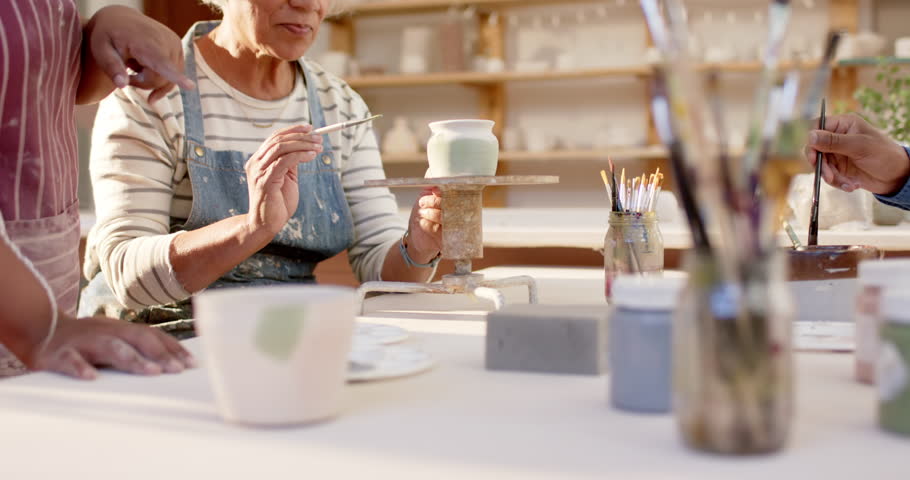 Happy diverse group of potters glazing clay jugs and discussing in pottery studio. Pottery, ceramics, handmade, local business, hobbies and craft, teamwork, unaltered.