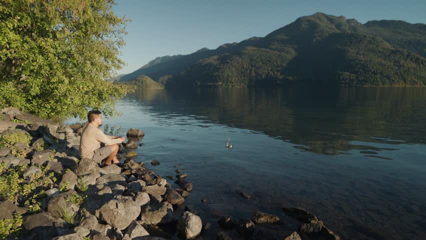 Man Sit Daydream Throwing Small Rock on Lake Crescent a deep beautiful pristine waters lake in Olympic National Park