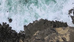 Sliding movement with Top down view of rocky coastline with powerful sea waves leading up to it. Watu Lumbung beach, Gunung Kidul, Indonesia - 4K drone shot
