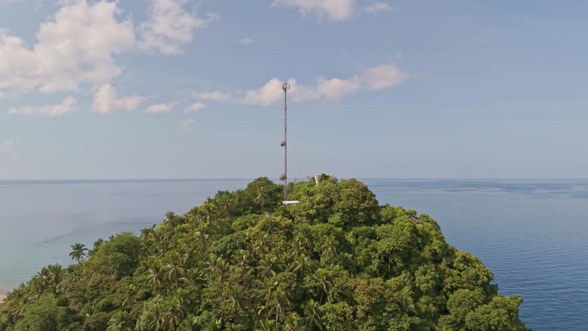 A cell tower on top of a jungle covered hill, with views over the vast coastline and mountainous landscape. Jubgan, Surigao Del Norte, Philippines. Aerial Drone shot, daytime. 
