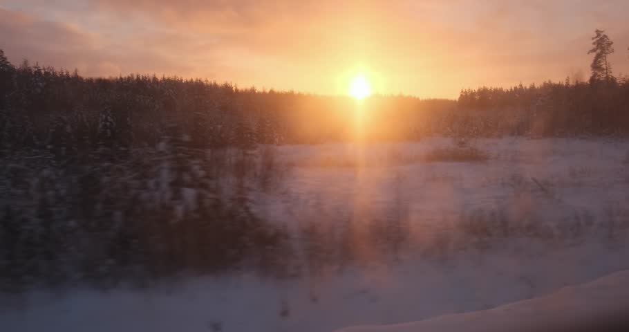 The train's window captures the dance of sunset hues on snow-clad woods, painting a winter dream.
