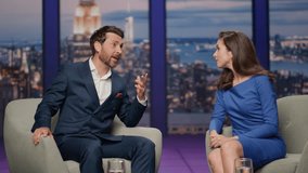 Talk show guest sharing success to audience sitting television studio with attractive host. Smiling woman presenter listening man speaking reacting emotionally. Happy businessman telling story on air. - Powered by Shutterstock - Get 15% off with code: PIKWIZARD15