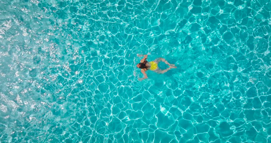 Aerial view of a woman in yellow swimsuit swimming in the pool. Summer lifestyle