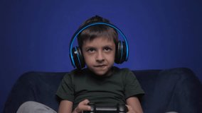 child a boy of six years old is sitting on the armchair at home in wireless headphones in the evening and playing video games with a black joystick - Powered by Shutterstock - Get 15% off with code: PIKWIZARD15