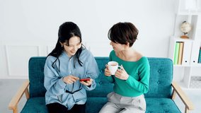 Two Asian women chatting while looking at their smartphone.