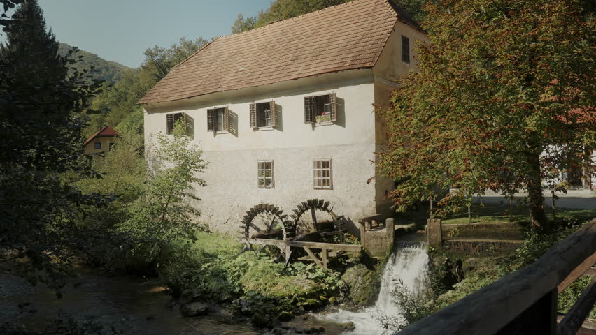 Traditional old house by the river. The mill wheel rotating under the stream of water in the village.  Stream of flowing water turning an old wooden mill. 