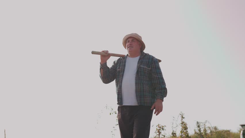 Farm Life in 4K An Aged Farmer Takes a Relaxing Walk in the Outdoors, His Trusty Shovel at Hand. Farming Dedication Mature Man and His Trusty Shovel