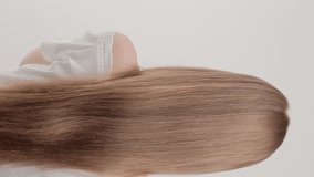 Vertical video. A red-haired girl stands with her back in the studio on a gray background and waves her hair. The concept of caring for beautiful and healthy hair. - Powered by Shutterstock - Get 15% off with code: PIKWIZARD15
