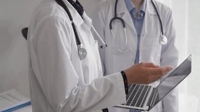 Two doctors are using a laptop computer while standing and discussing health treatment in a hospital. Medicine concept