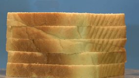 Sliced toasted white bread stack rotating on blue background, wooden slicing board, looped video.