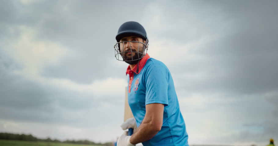 Portrait of a Professional Cricket Player in Blue Uniform and Protective Helmet Preparing to Hit the Ball and Defend the Wicket. Rainy Weather and Handheld Low Angle Camera Create a Dramatic Effect Royalty-Free Stock Footage #1110455005