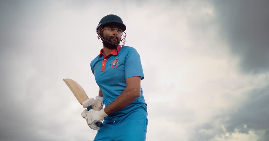 Professional Indian Cricket Player Striking the Ball with a Bat. Batter From a Blue Team Successfully Hits the Ball to the Outfield. Low Angle Action Footage on a Cloudy Day Royalty-Free Stock Footage #1110455015