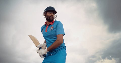 Professional Indian Cricket Player Striking the Ball with a Bat. Batter From a Blue Team Successfully Hits the Ball to the Outfield. Low Angle Action Footage on a Cloudy Day Stock Video