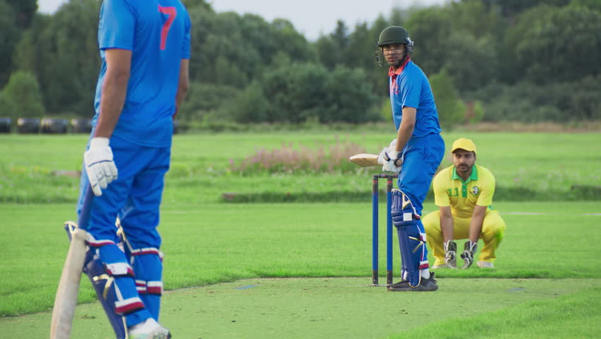 Cricket Batsman Striking the Ball and Sprinting Across the Pitch. Opponent Yellow Team Manages to Hit the Wicket Before the Runner Finishes the Scoring Run. Two Premier Indian Teams Playing a Game