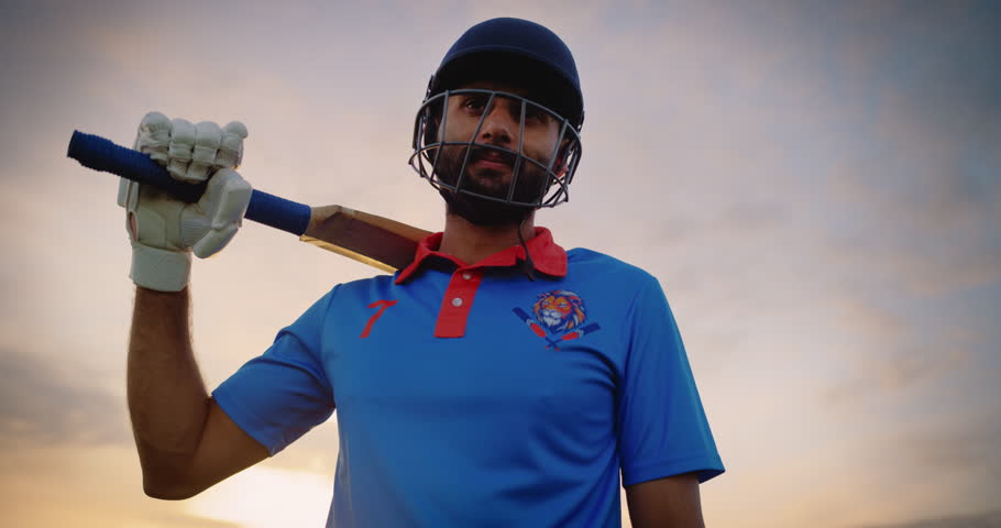 Zoom In Portrait of a South Asian Cricket Player Standing on a Pitch in Blue Uniform and a Protective Helmet. Professional Indian Athlete Looking at Camera, Smiling and Enjoying the Day
