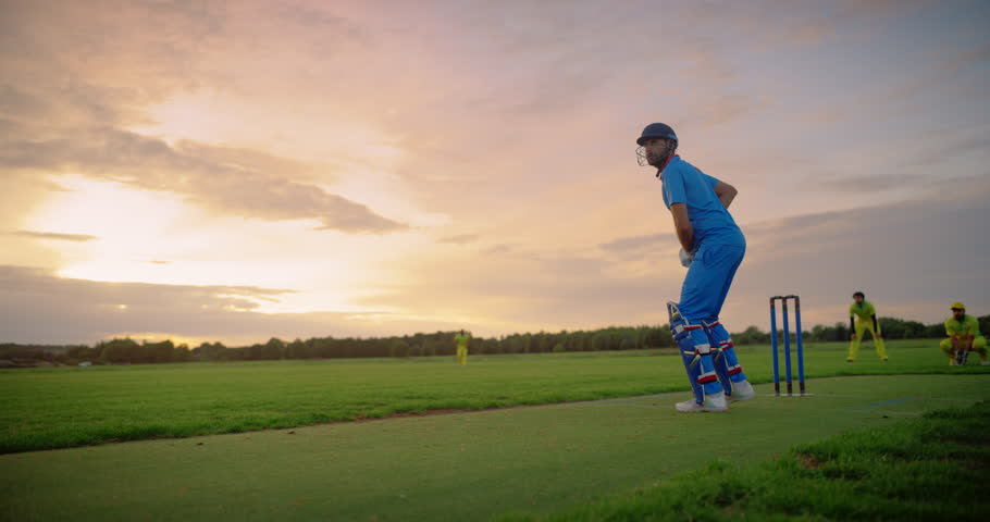 Portrait of an Athletic Indian Cricket Player Striking the Ball with a Bat. Batter From a Blue Team Sends the Ball to the Outfield and Completes a Run. Handheld Slow Motion Action Footage