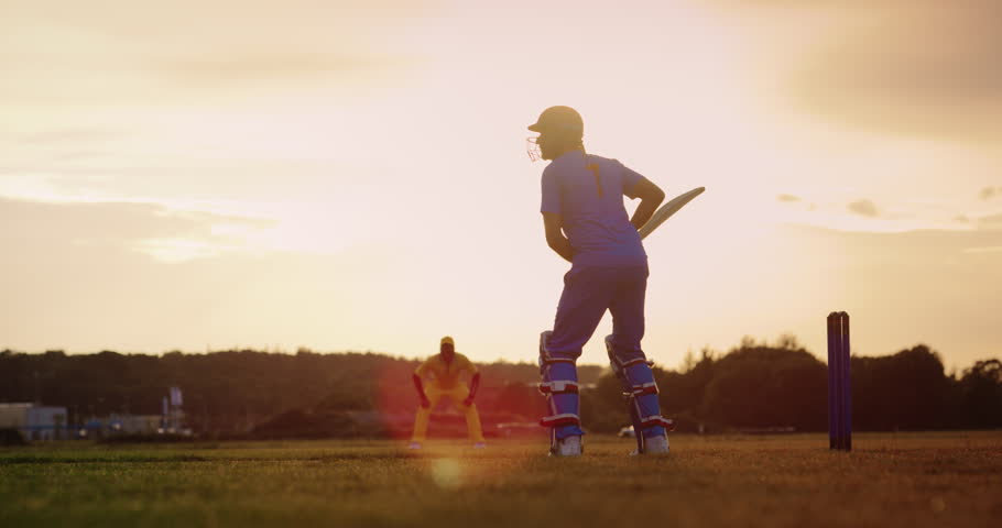 Professional Indian Cricket Player in Blue Uniform and Protective Gear Hitting the Ball and Defending the Wicket. Athletes Practicing on a Green Field on a Sunny Afternoon. Cinematic Slow Motion