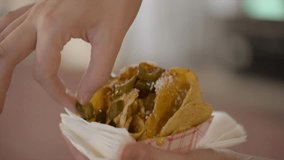 This close up video shows a hand holding vendor cheese nachos and picking a pepper off.