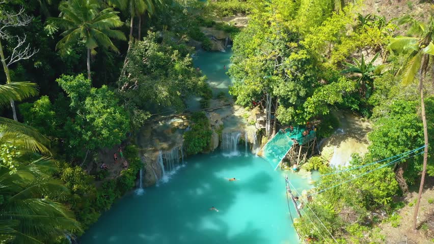Cambugahay falls, Siquijor island, Philippines. Slow aerial travelling. Cinematic drone view. Filipino tourists swimming and playing in the turquoise waterfall lagoons. Famous travel destination. Royalty-Free Stock Footage #1110465303