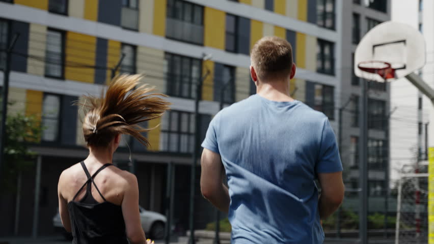 Athletes from the back. A man and a girl play sports on a basketball court.