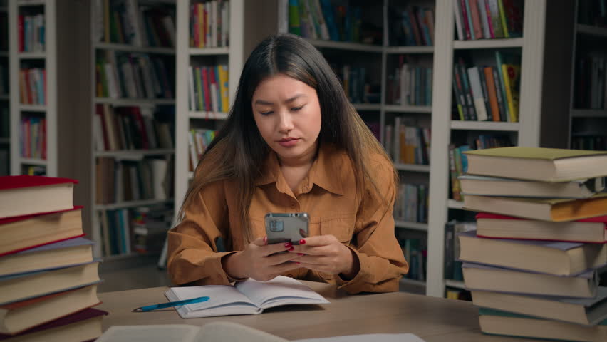 Sad frustrated stressed asian woman girl in university library checking email reading bad news on mobile phone disappointed chinese female student getting notification failing exam losing scholarship Royalty-Free Stock Footage #1110475107
