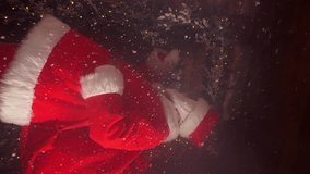 Santa Claus knock door under snow fall for visit children and giving wished traditional presents for happy holiday on Christmas Eve night. Vertical video format