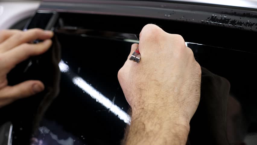 The car mechanic cuts off the excess tinting foil when gluing on the car glass in the garage. Installing car window tint. Royalty-Free Stock Footage #1110482079