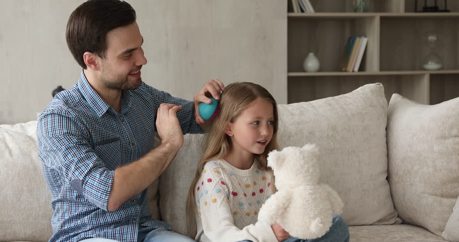 My baby princess. Caring single dad sit on sofa brush hair of junior school age daughter talk chat with kid enjoy spending time together. Foster father make hairstyle to little adopted girl at morning Royalty-Free Stock Footage #1110482459