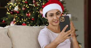Overjoyed millennial Indian female hold video call shoot New Year greeting on smartphone speak Christmas toast hold glass of champagne. Happy young woman celebrate Xmas online greet friends remotely