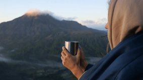 Close-up of woman wrapped in blanket holding hot coffee, enjoying view of mountains Cinematic video of mountains with peaks in clouds, camping traveler Spend weekend in camping, meet dawn in mountains