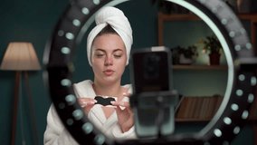 Woman beauty blogger shoots cosmetic vlog looks at camera of smartphone, applying black cleansing nose mask for acne talks with followers, records video broadcast.